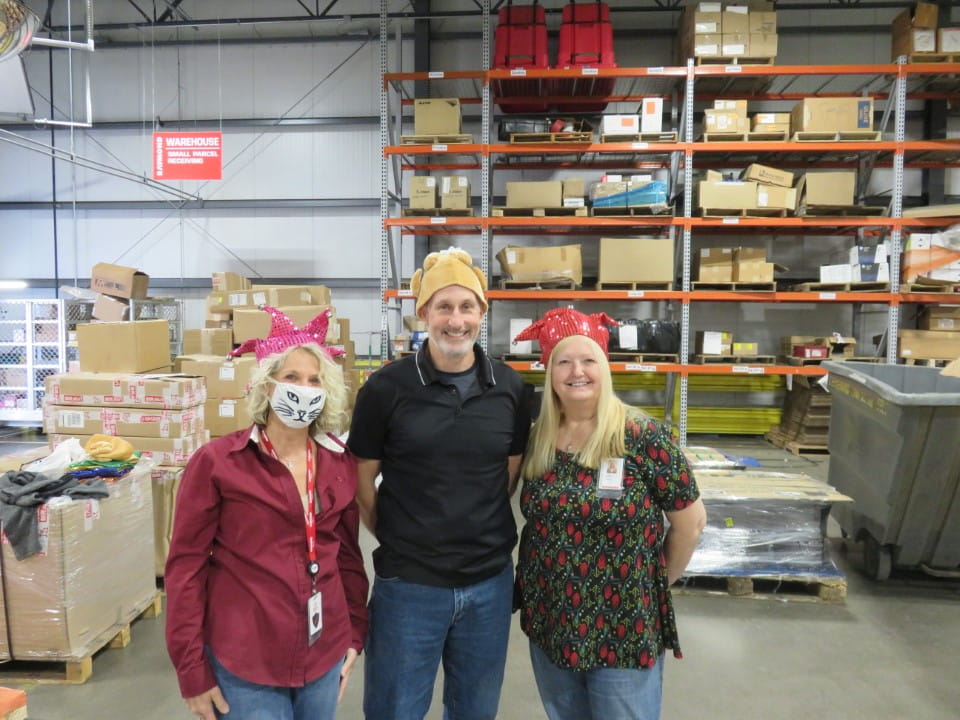 Three employees stand together while smiling on turkey delivery day. 
