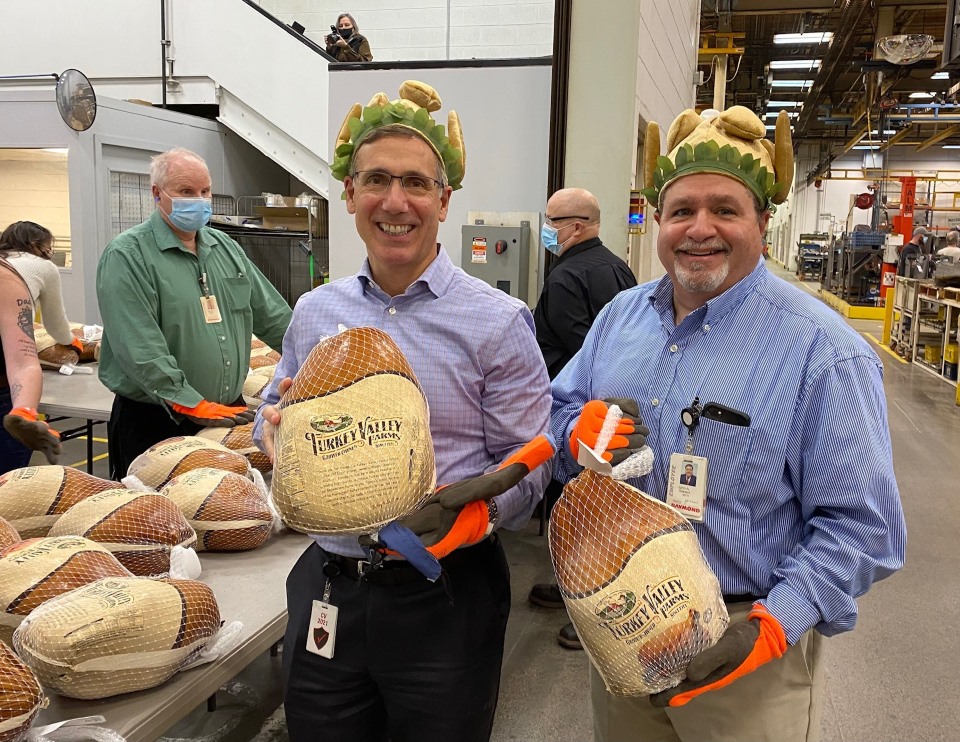 2 people from Raymonds management team holding frozen turkeys with festive thanksgiving turkey hats on. 